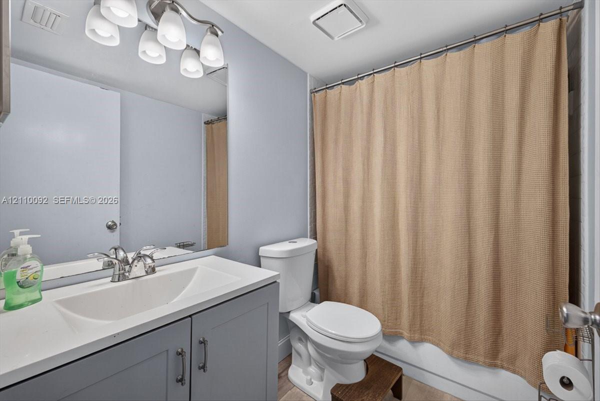 Bathroom featuring a vanity with a white integrated basin, charcoal-toned cabinetry, a polished chrome faucet, and a multi-bulb light fixture above a wall-mounted mirror