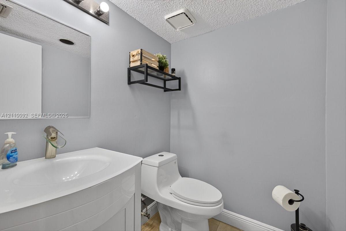 Wall-mounted rectangular vanity with a white integrated basin, single-handle brushed nickel faucet, large frameless mirror, and dual-flush toilet