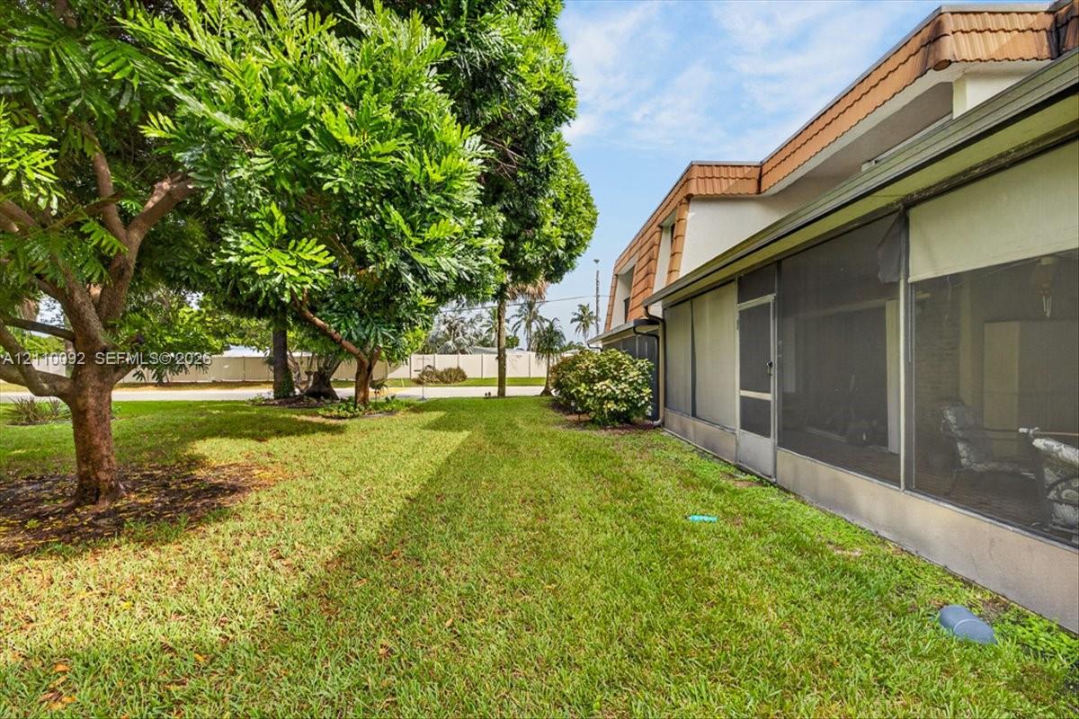 Exterior side yard featuring a manicured lawn, mature trees, and a screened-in enclosure with metal framing