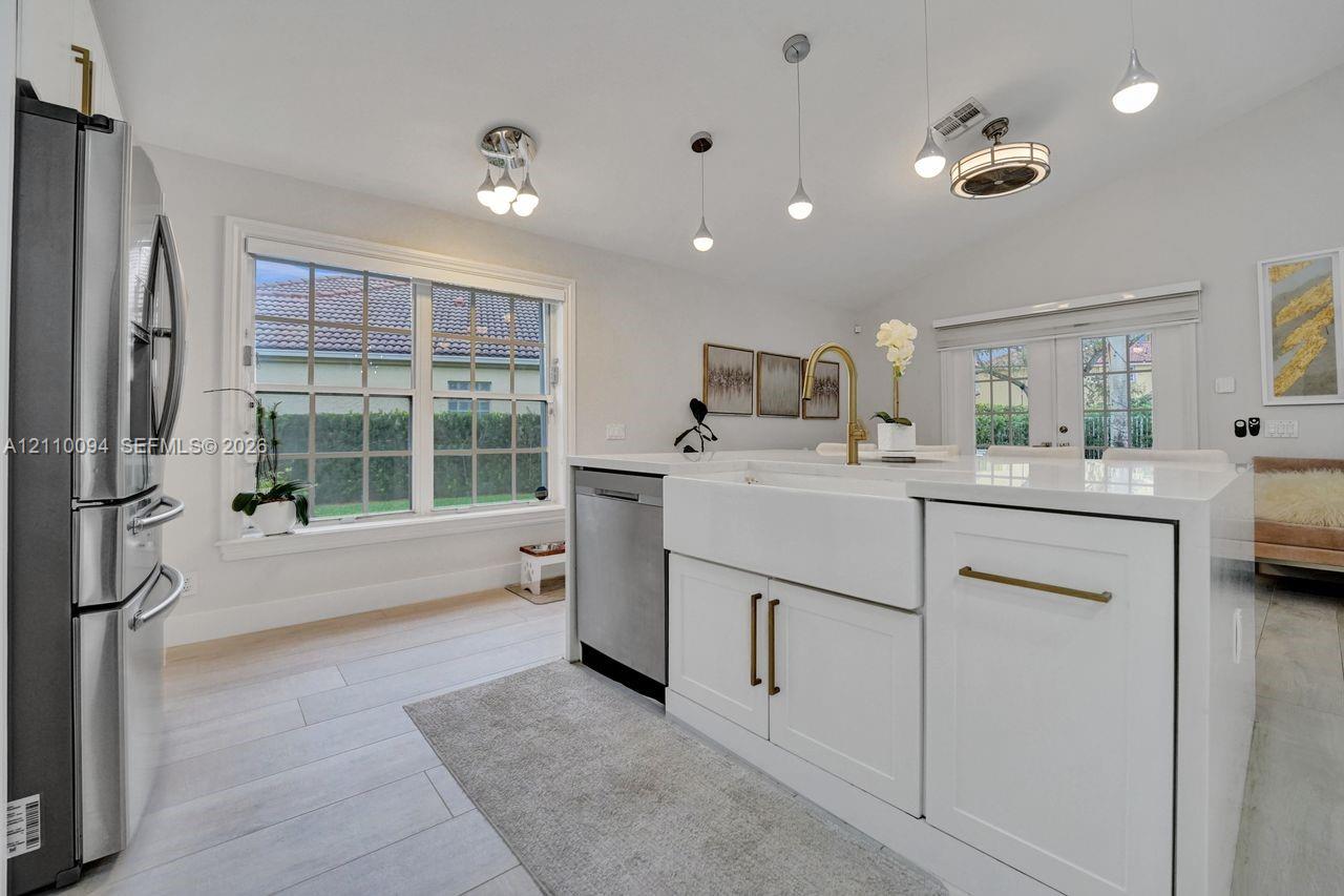 Kitchen featuring an island with a white farmhouse sink, brass-tone hardware, stainless steel appliances, pendant lighting, and wood-finish flooring
