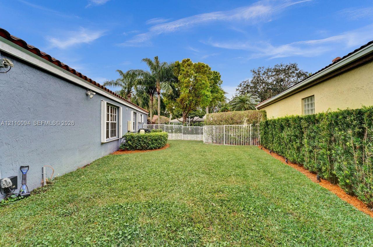 Side yard featuring a grass lawn, metal fencing, stucco exterior walls, and manicured hedge landscaping