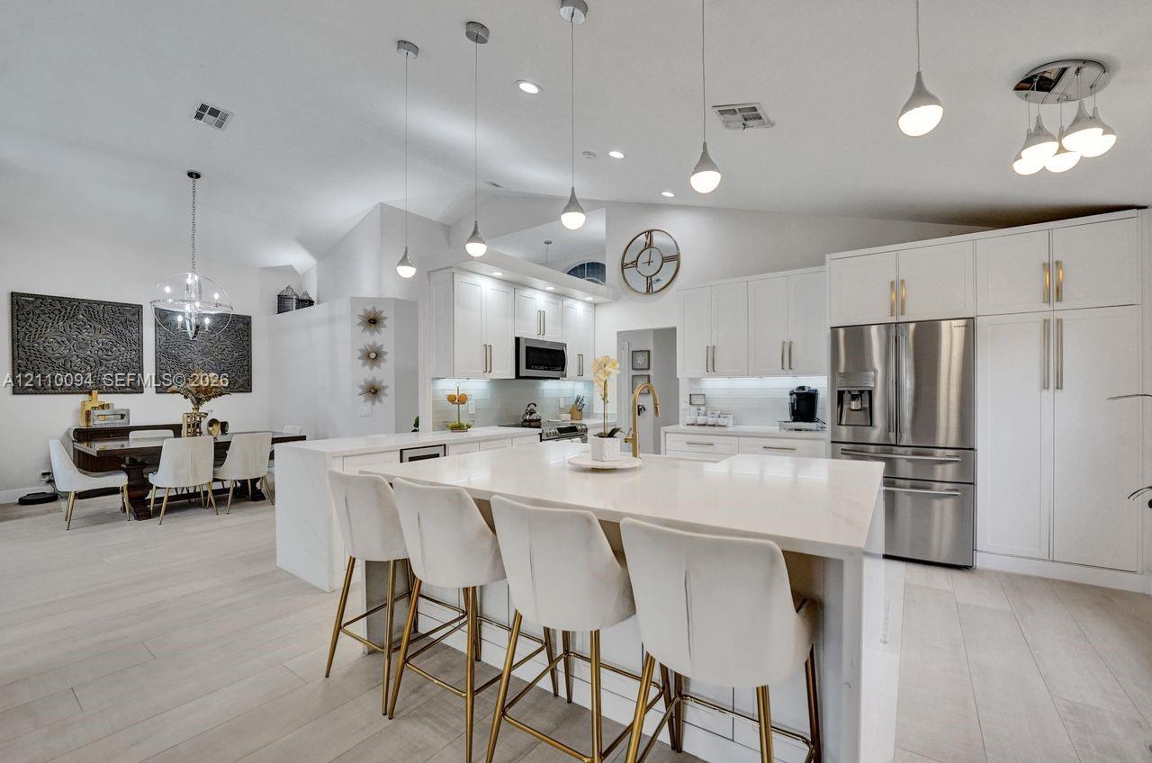 Kitchen featuring white shaker cabinetry, a waterfall-edge center island with stone countertop, stainless steel appliances, recessed lighting, and wood-finish flooring