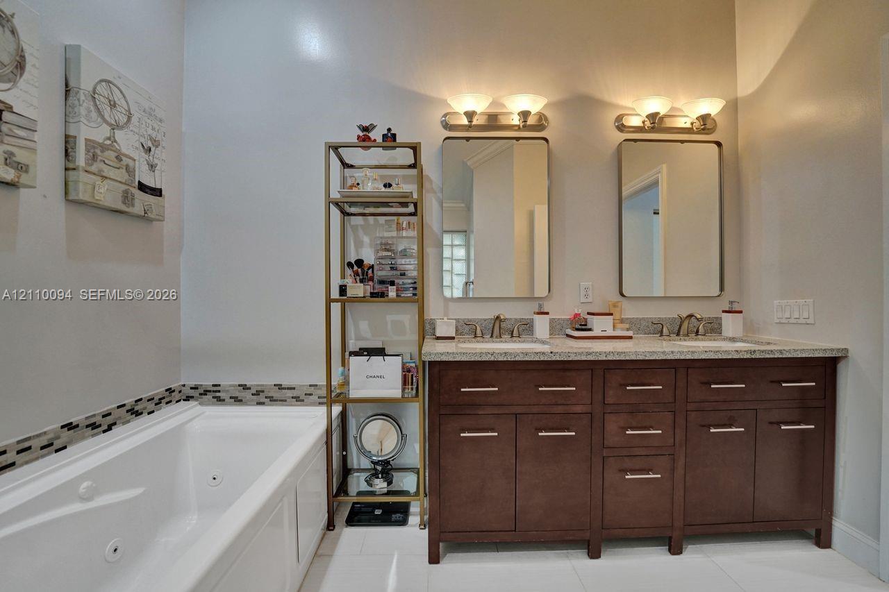 Double-sink vanity featuring dark wood-finish cabinetry, stone-composite countertop, dual rectangular mirrors, and polished metal lighting fixtures, paired with a jetted soaking tub featuring an integrated tile backsplash