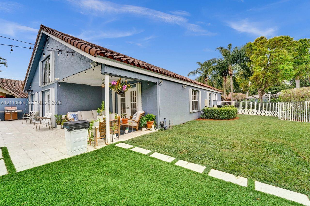 Stucco exterior with a tiled roof, covered patio featuring paved hardscaping, and a fenced backyard with a manicured lawn