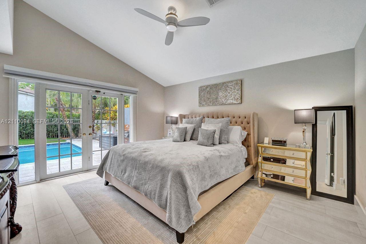 Vaulted ceilings, wood-finish flooring, and white-framed French doors opening to an exterior swimming pool
