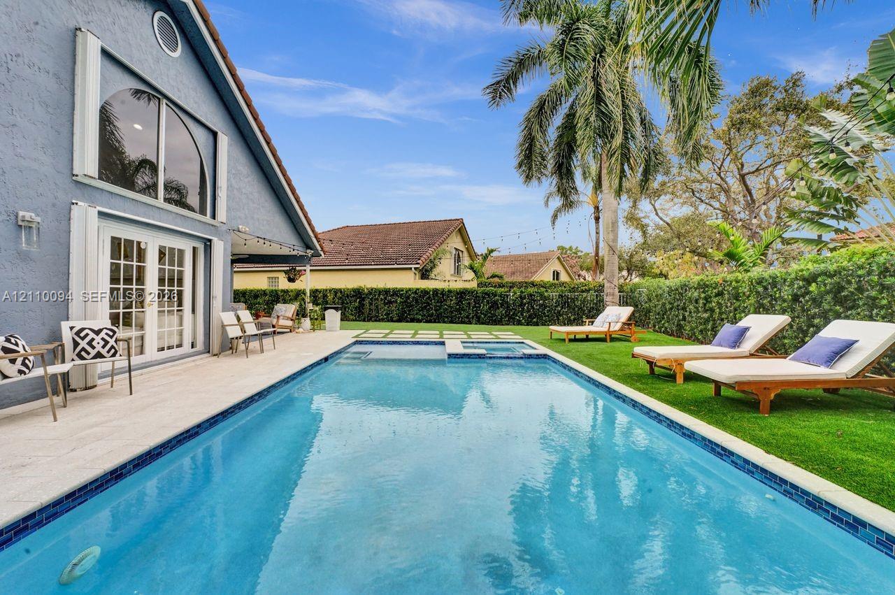 Backyard featuring a rectangular swimming pool with a tiled waterline, integrated spa, stone-finish deck, manicured lawn, and mature palm tree