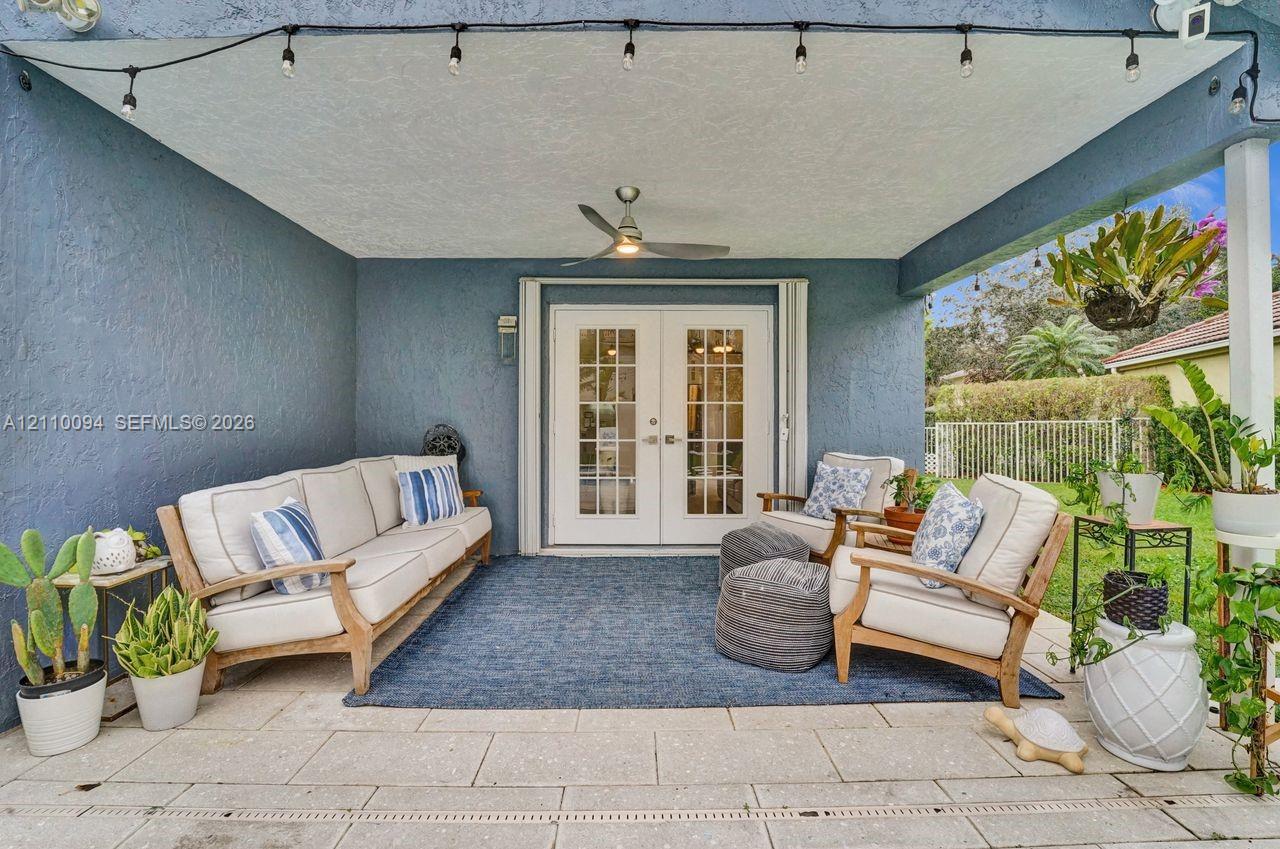 Covered patio featuring stone-tiled flooring, white French doors, a central ceiling fan, and perimeter string lighting