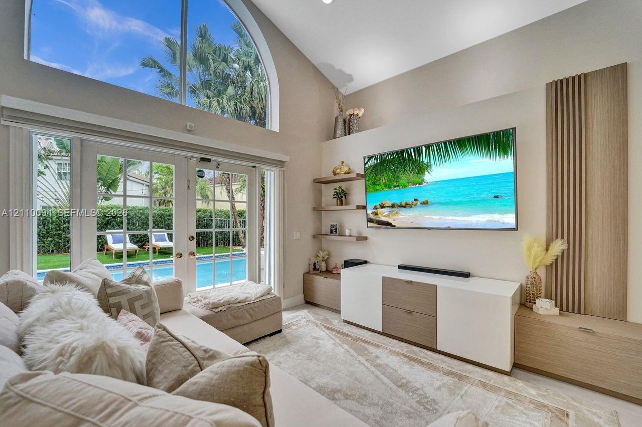 Vaulted ceilings featuring an arched transom window, custom wood-slat wall paneling, built-in cabinetry, floating shelving, and French doors
