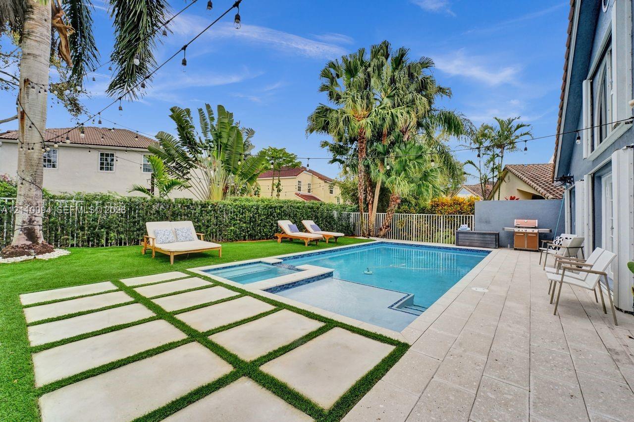 Backyard featuring an in-ground swimming pool with an integrated spa, large-format paver patio, square concrete pavers set in turf, and mature palm trees
