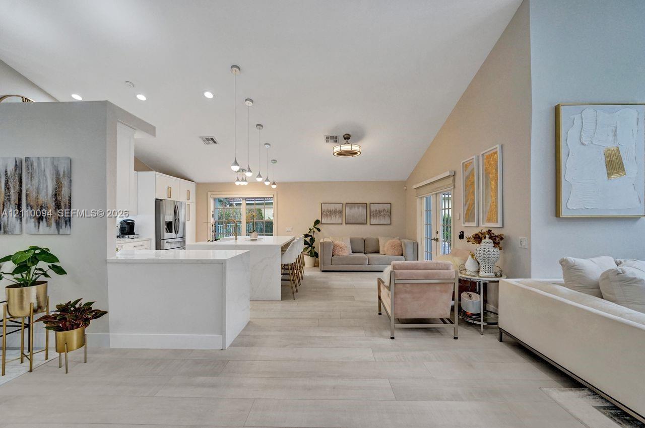 Open-concept interior featuring vaulted ceilings, recessed lighting, wood-finish flooring, a kitchen island with stone-style countertops, and pendant lighting