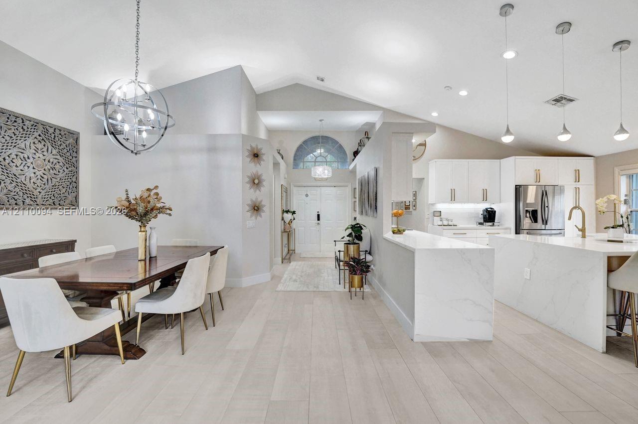 Vaulted ceilings with recessed lighting, wood-finish flooring, a kitchen island with stone-finish waterfall edges, white cabinetry, and a spherical metal chandelier