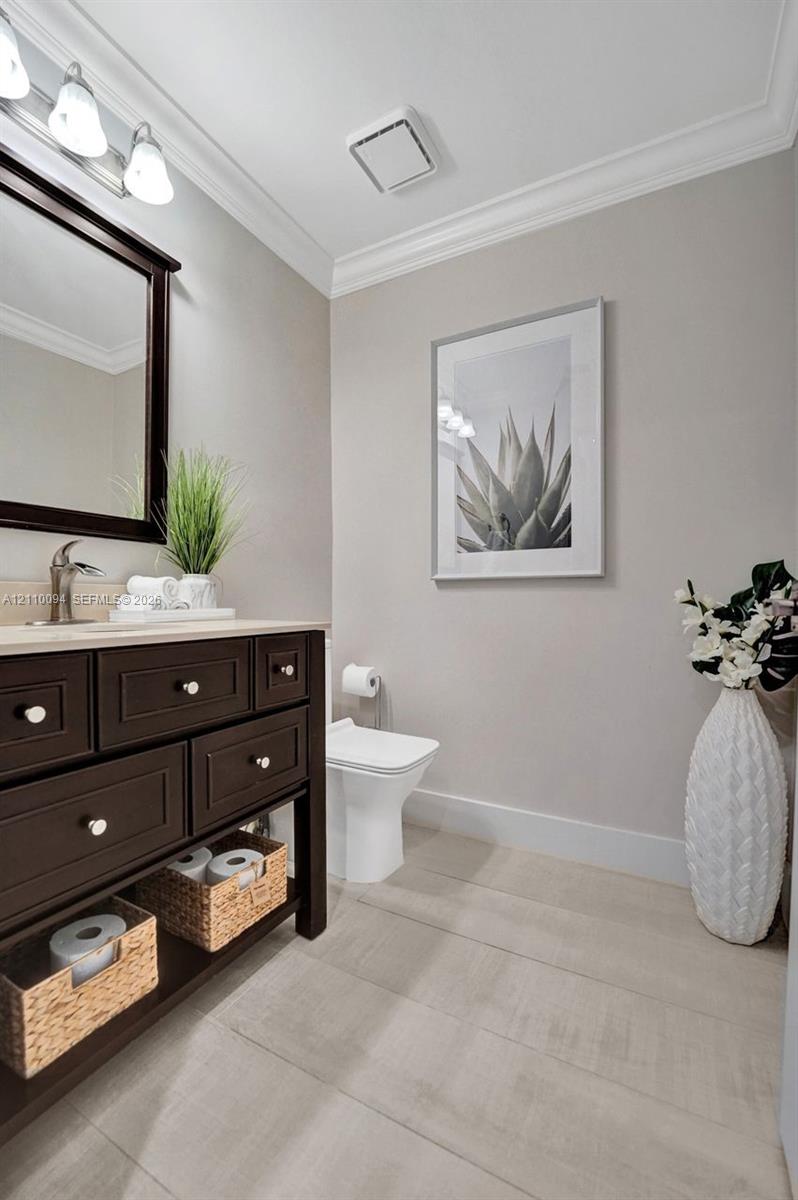 Dark-finish vanity cabinet, neutral stone-top surface, brushed metal faucet, three-bulb vanity lighting, and crown molding