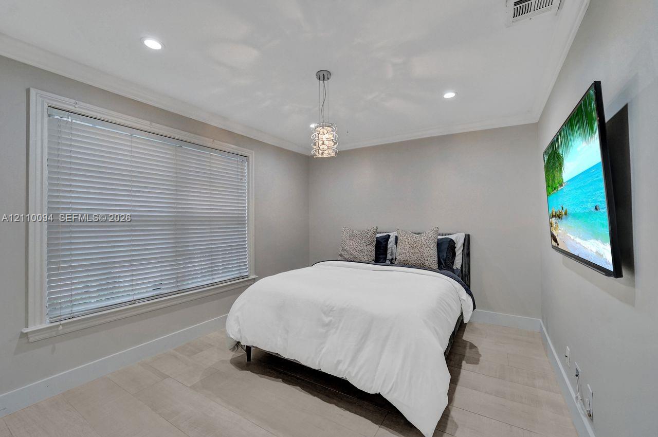 Neutral interior featuring light-toned tile flooring, crown molding, recessed lighting, a modern crystal pendant light fixture, and horizontal window blinds