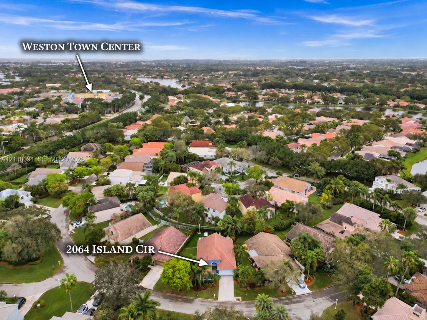 Aerial perspective of a single-family residence featuring a tiled roof and concrete driveway, situated within a suburban neighborhood with mature trees and proximity to Weston Town Center Aerial perspective of a single-family residence featuring a tiled roof and concrete driveway, situated within a suburban neighborhood with mature trees and proximity to Weston Town Center