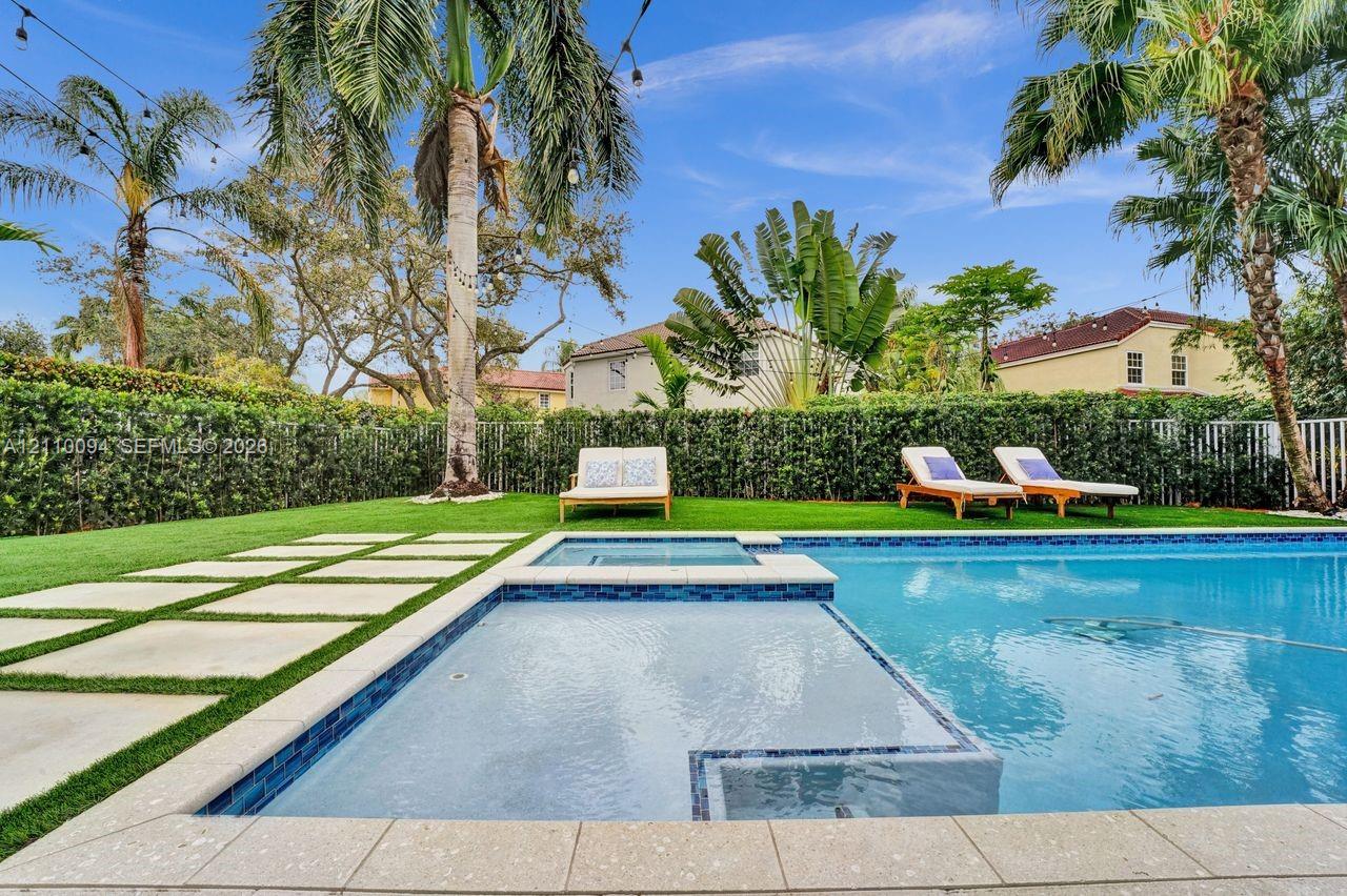 In-ground swimming pool with an integrated spa, stone-paver decking, manicured lawn, and perimeter privacy hedging