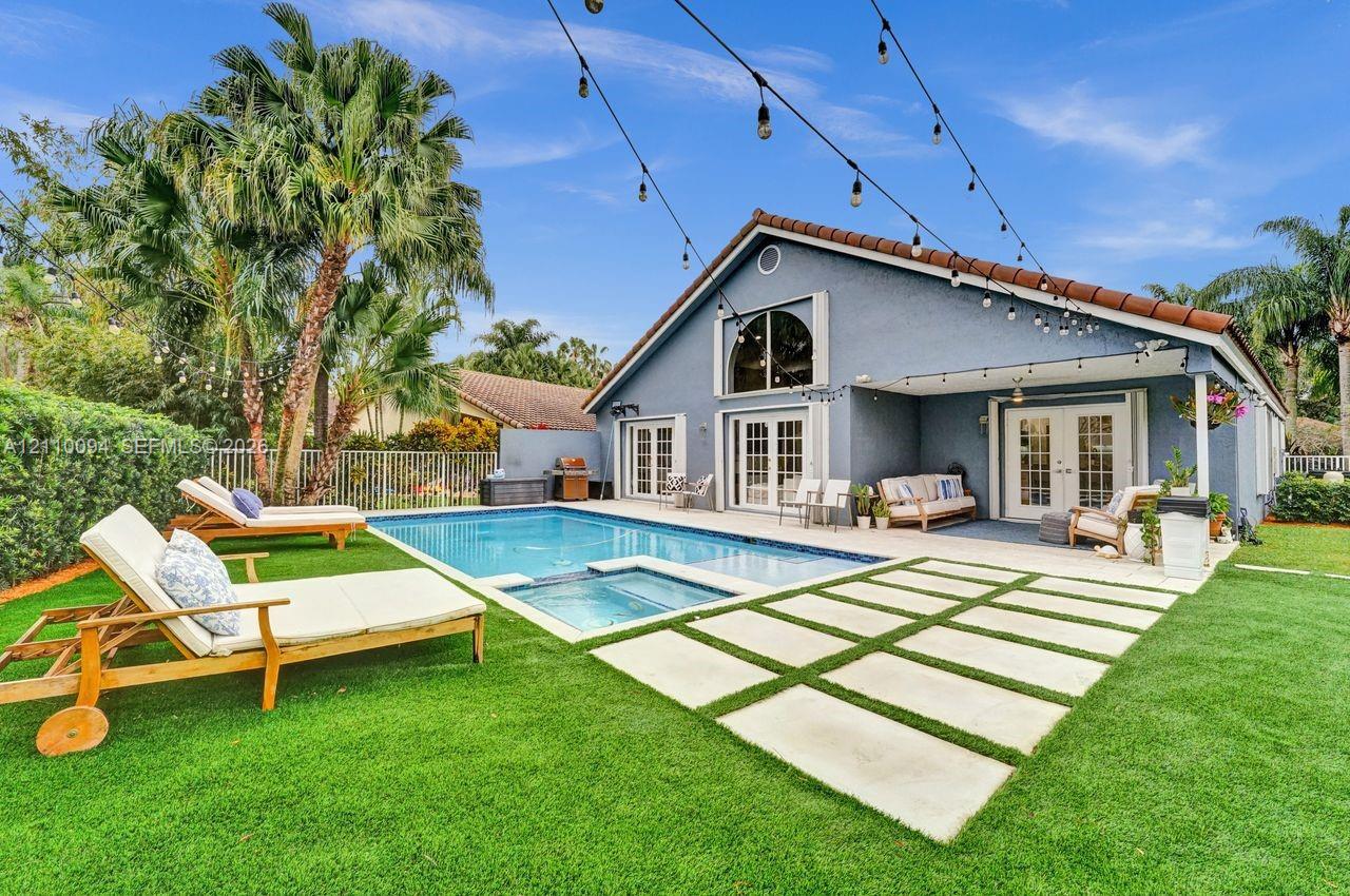 Backyard oasis featuring an in-ground pool with an integrated spa, concrete paver patio, covered porch, and mature palm trees Backyard oasis featuring an in-ground pool with an integrated spa, concrete paver patio, covered porch, and mature palm trees