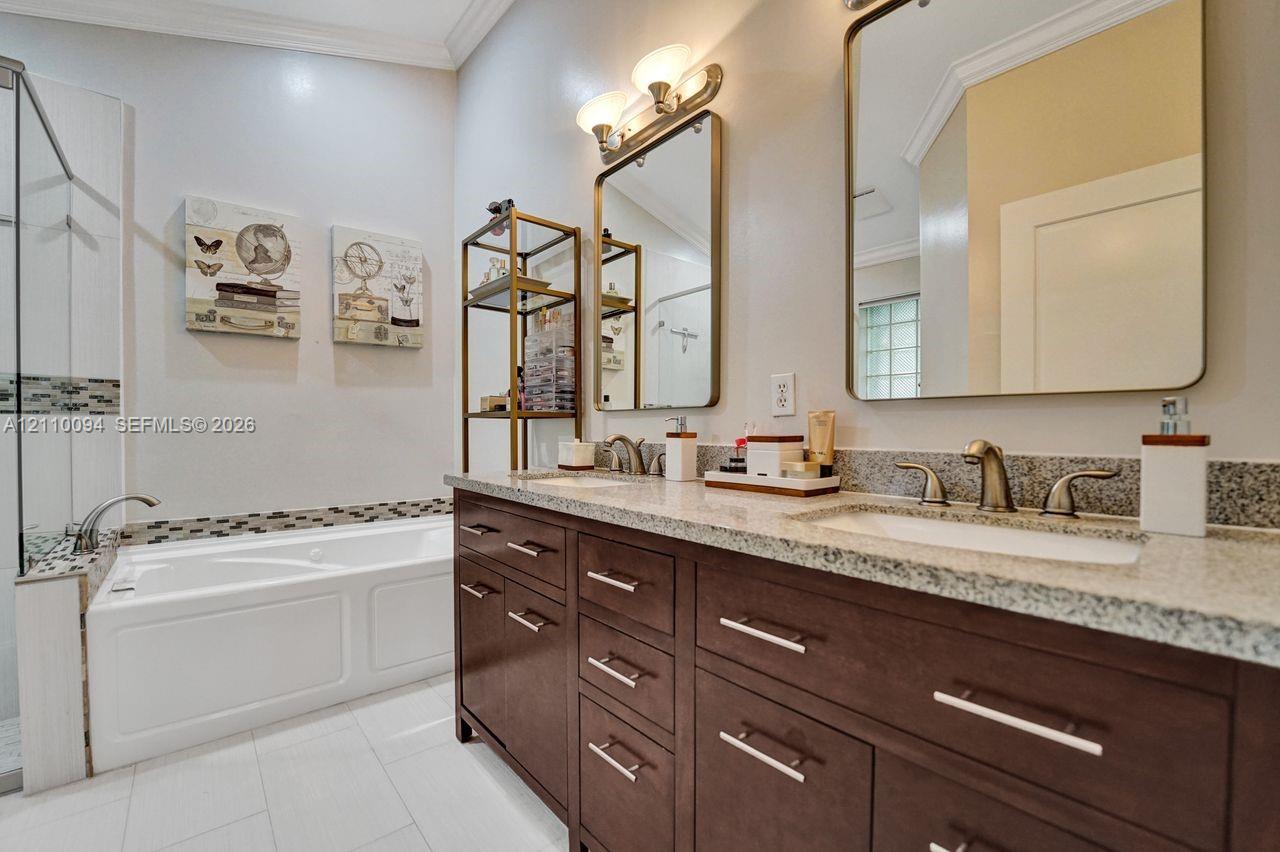 Dual-sink vanity with dark wood-finish cabinetry, stone-composite countertops, rectangular undermount sinks, and metallic hardware, featuring a deep soaking tub with a tiled surround and ceramic floor tile