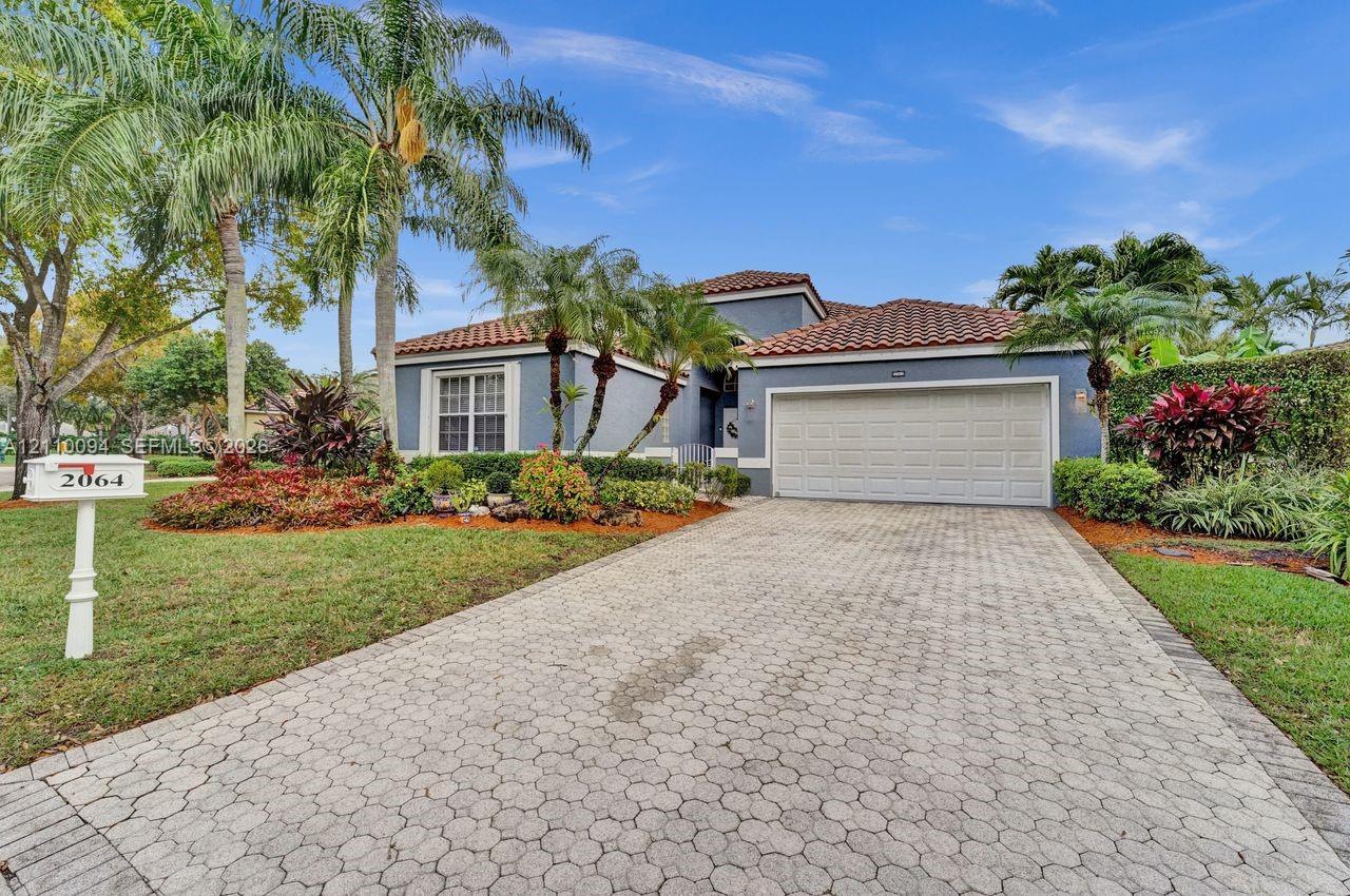 Exterior facade featuring a tiled roof, multi-car garage, and paver driveway, complemented by mature tropical landscaping Exterior facade featuring a tiled roof, multi-car garage, and paver driveway, complemented by mature tropical landscaping