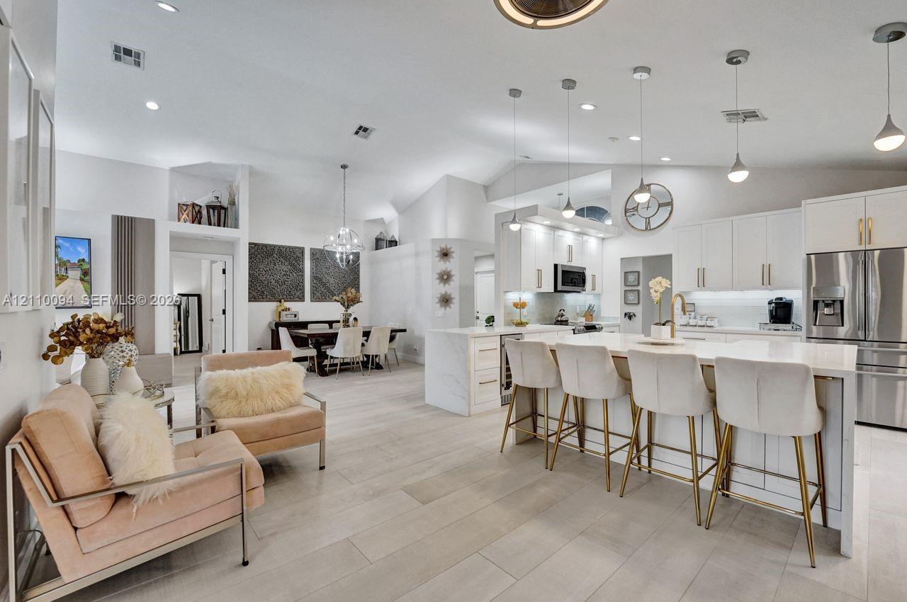 Open-concept living space featuring vaulted ceilings, wood-finish flooring, a kitchen island with stone-surface countertop, white shaker-style cabinetry, and recessed lighting
