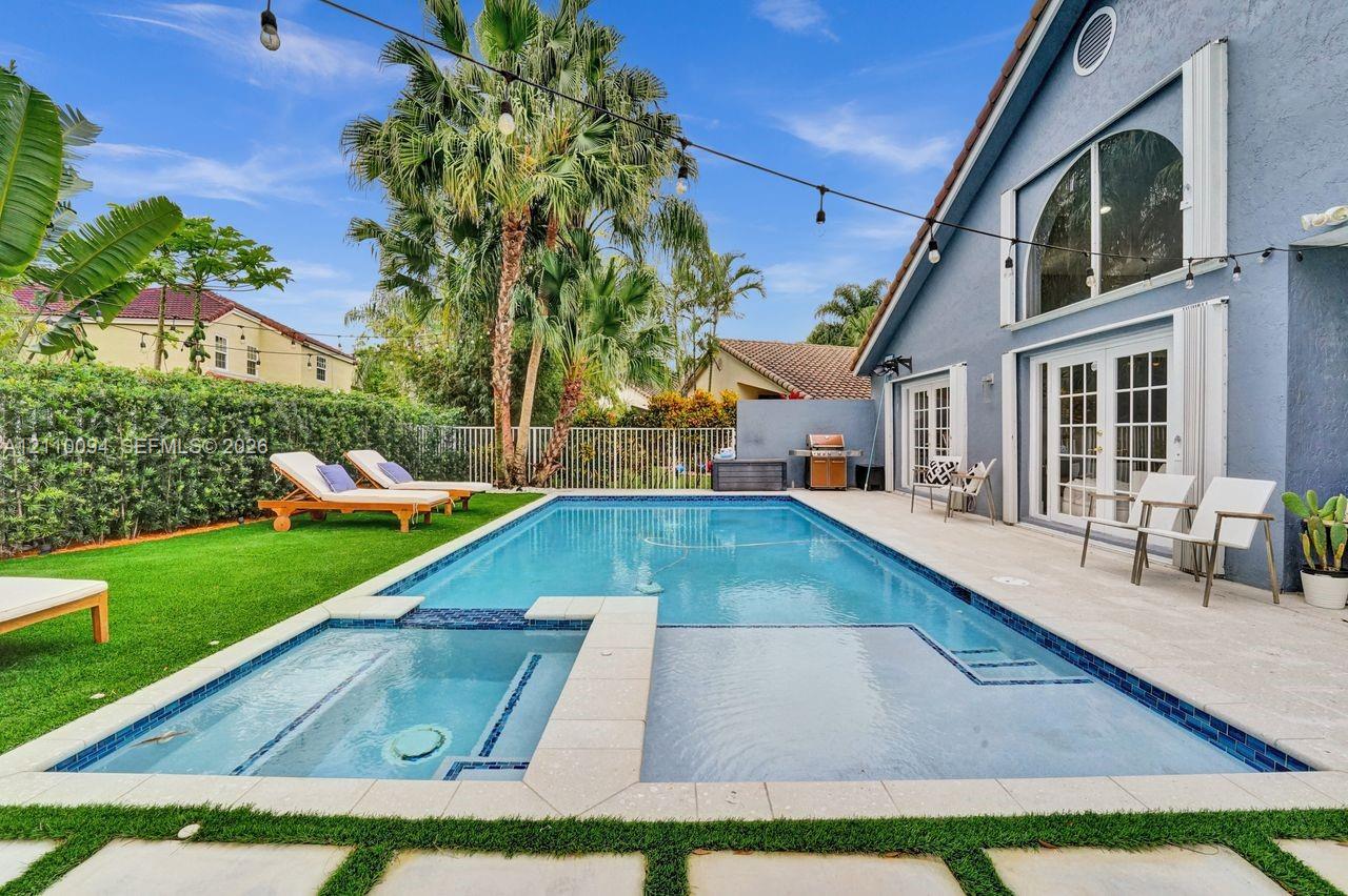 Backyard pool area featuring an integrated spa, stone-paver decking, artificial turf lawn, and arched window detailing on the exterior facade Backyard pool area featuring an integrated spa, stone-paver decking, artificial turf lawn, and arched window detailing on the exterior facade