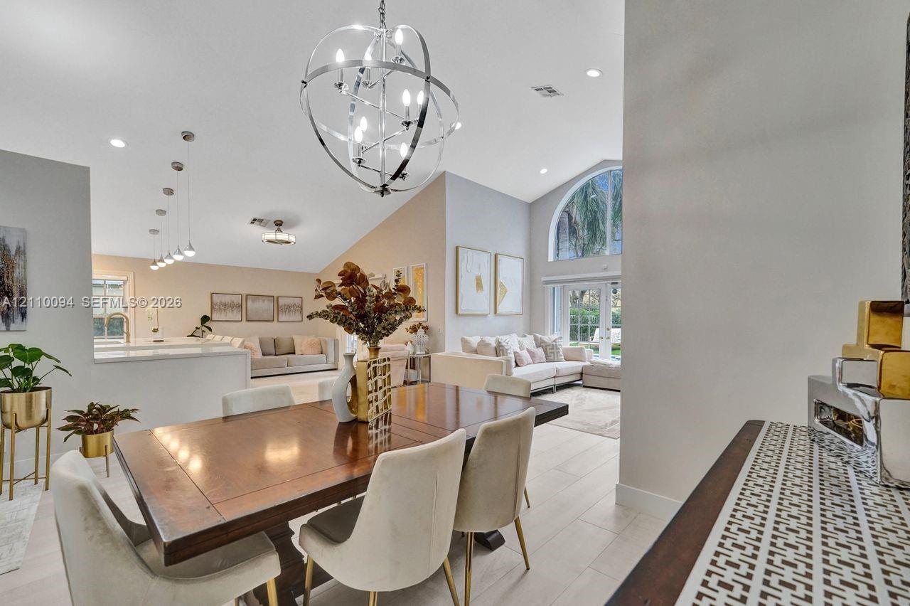 Vaulted ceilings, large arched window, spherical metallic chandelier, recessed lighting, and tile flooring