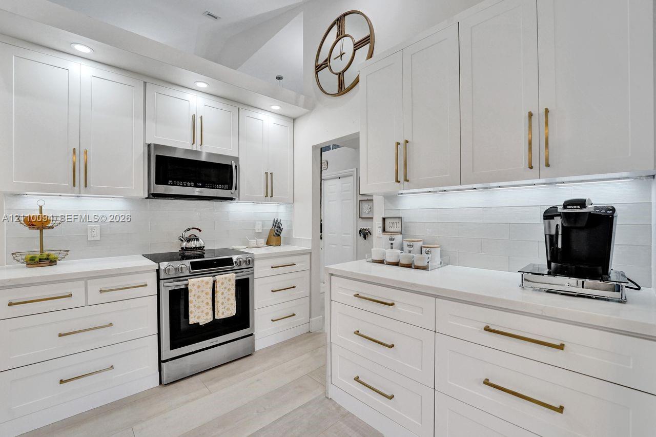 Kitchen featuring white shaker-style cabinetry, quartz countertops, subway tile backsplash, stainless steel appliances, and brushed brass hardware