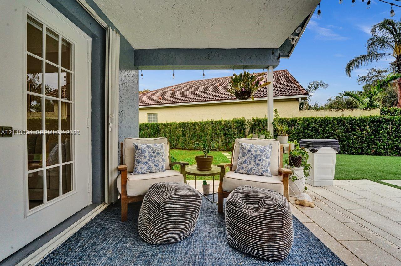 Covered patio featuring large-format stone pavers, white French door access, and a privacy hedge enclosure