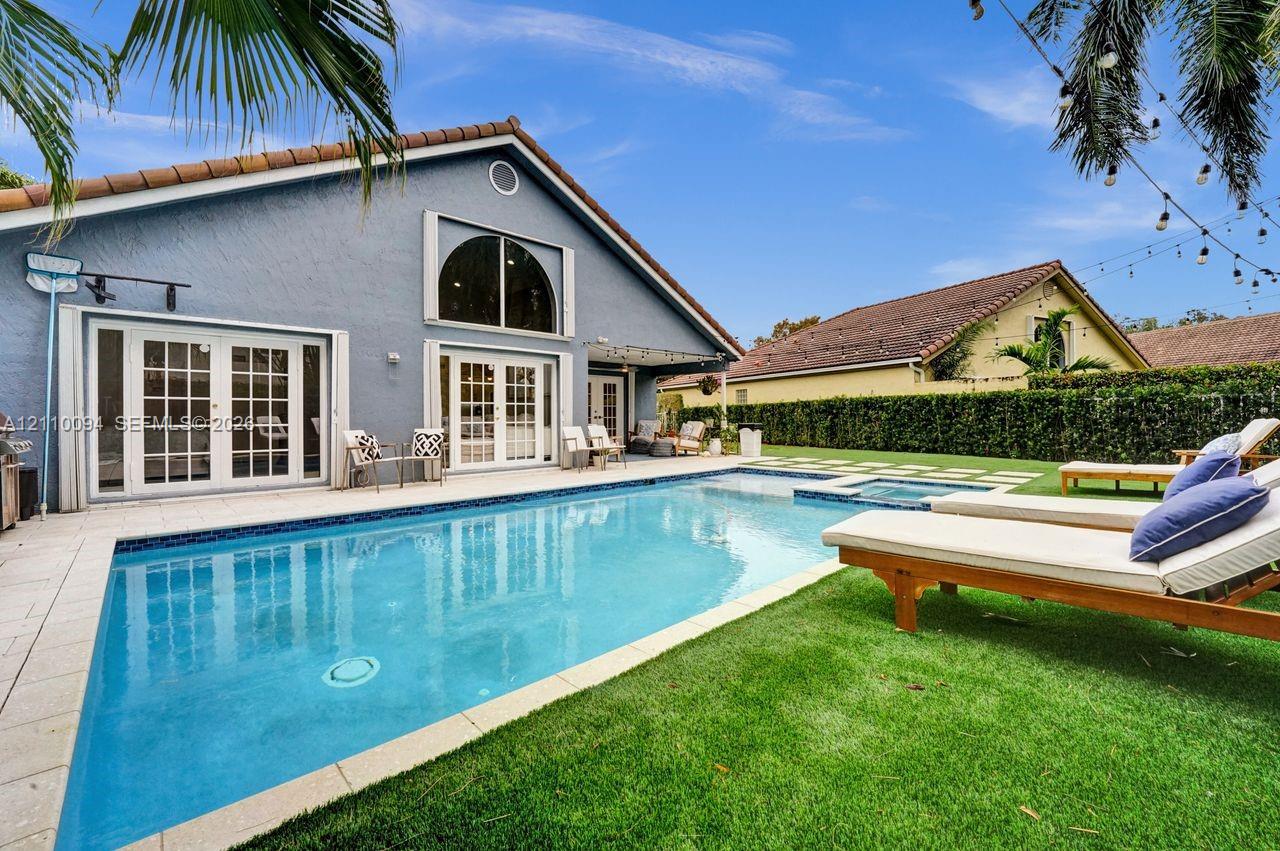 Stucco exterior featuring a multi-pane glass door entry, an in-ground swimming pool with an integrated spa, and a concrete patio