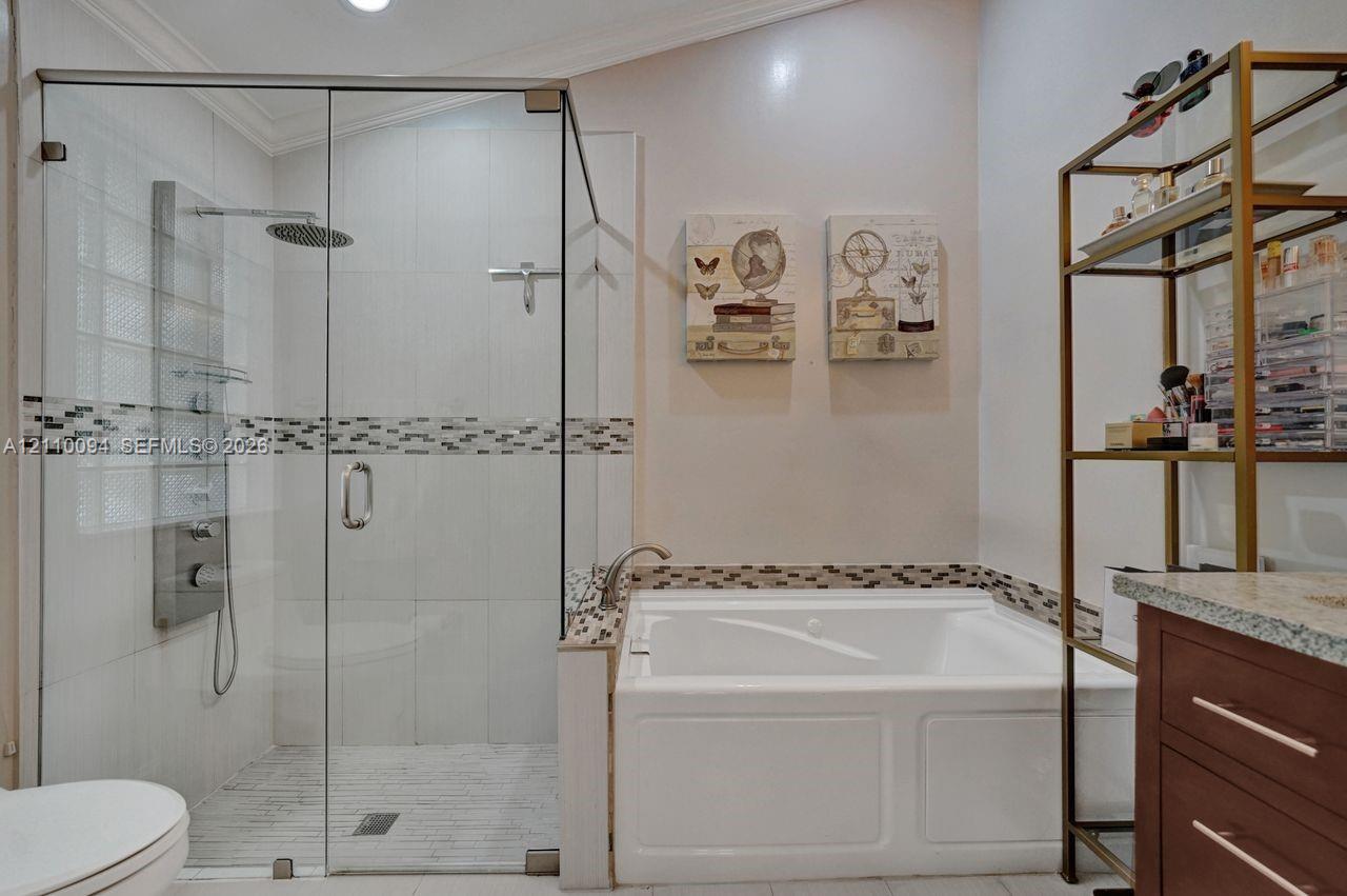Frameless glass shower enclosure with integrated rainfall shower head and body sprayers, soaking tub with a stone-composite surround, and decorative mosaic tile accents