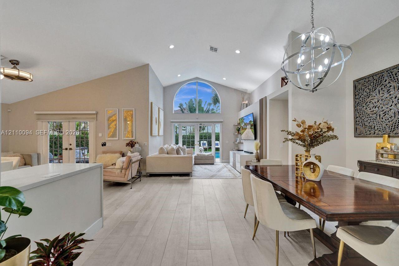 Open-concept interior featuring vaulted ceilings, wood-finish flooring, a prominent arched window, and a spherical metal chandelier