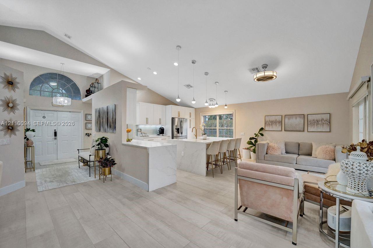 Open-concept interior featuring vaulted ceilings, a central kitchen island with waterfall-edge countertop, recessed lighting, and wood-finish flooring