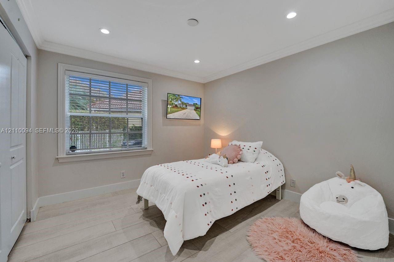 Neutral-toned bedroom featuring wood-finish flooring, recessed lighting, crown molding, and a multi-pane window with white blinds