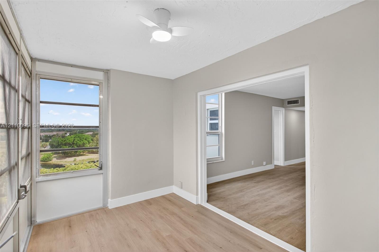Enclosed porch featuring wood-finish flooring, large window panels, and a ceiling-mounted light fixture with fan