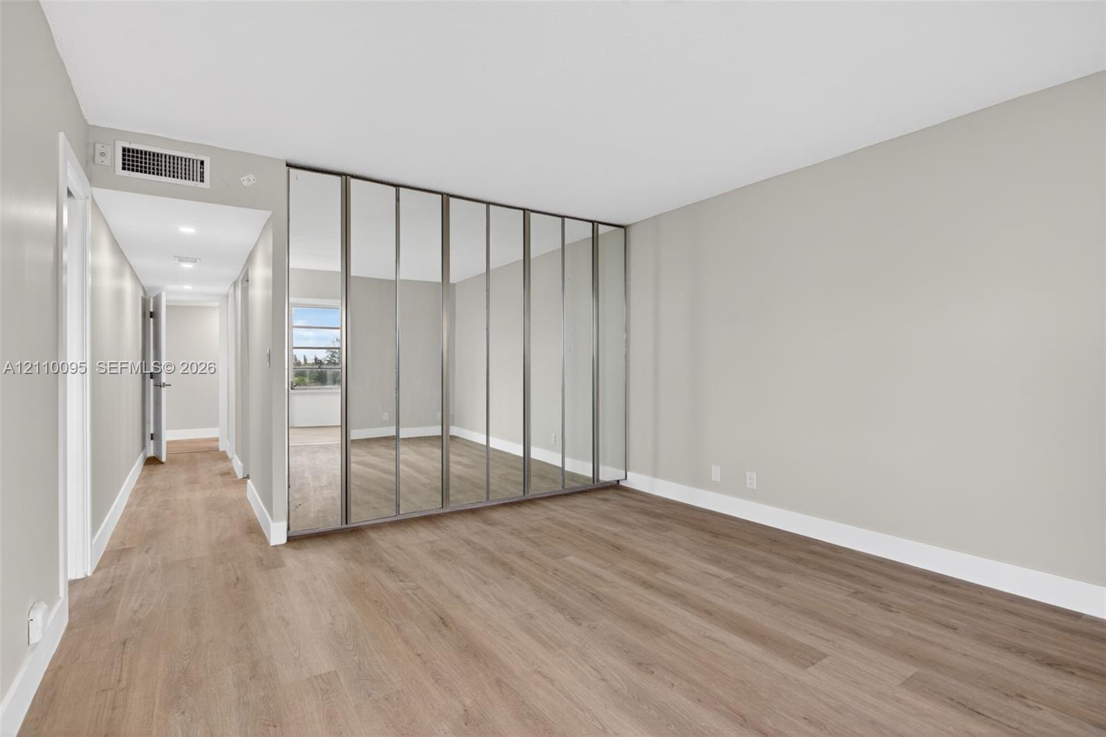 Full-height mirrored closet doors, neutral wall palette, wood-finish flooring, and recessed ceiling lighting