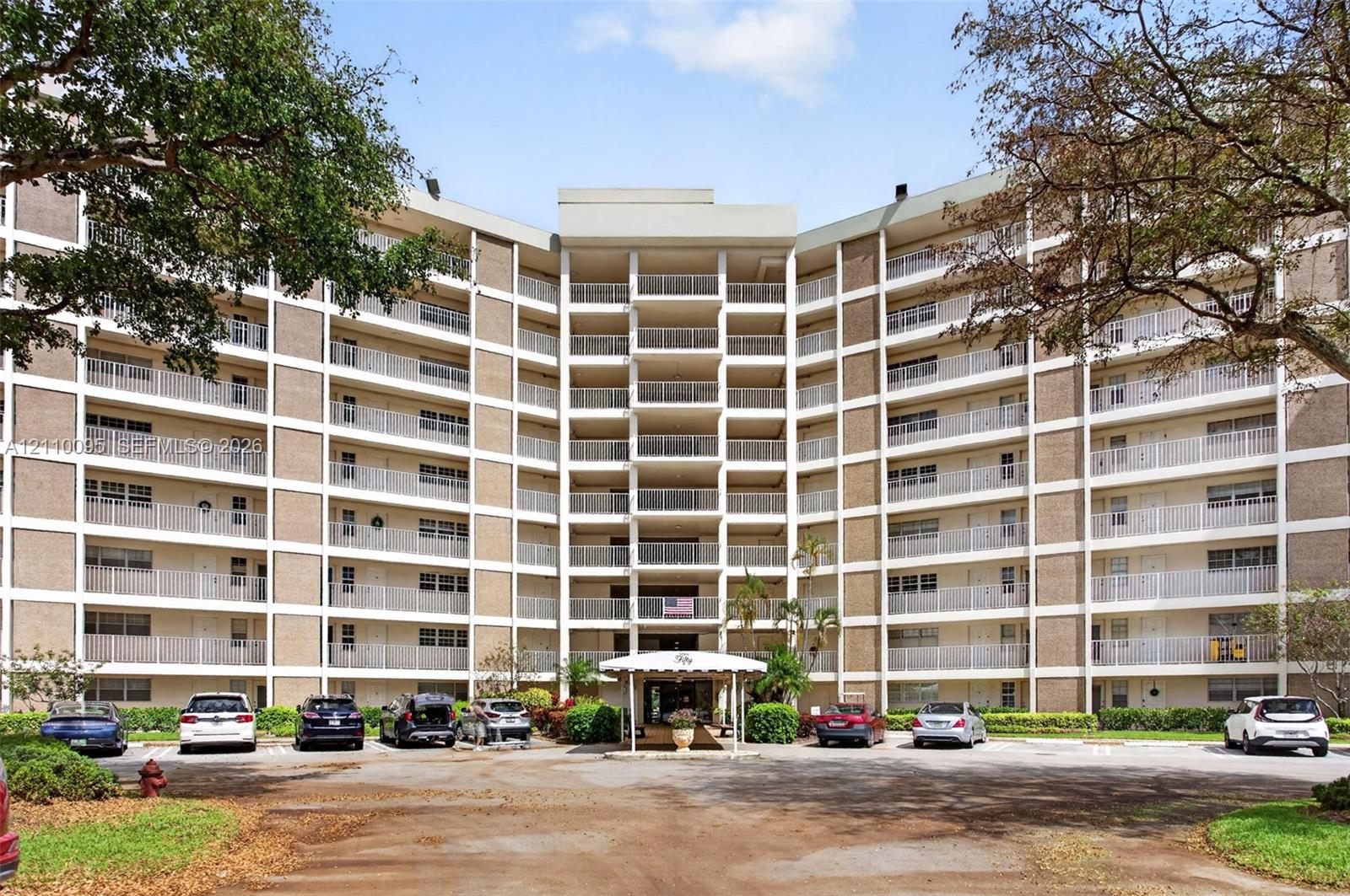Multi-story residential building exterior featuring a structured masonry facade, tiered private balconies with metal railings, and a covered ground-level entrance Multi-story residential building exterior featuring a structured masonry facade, tiered private balconies with metal railings, and a covered ground-level entrance