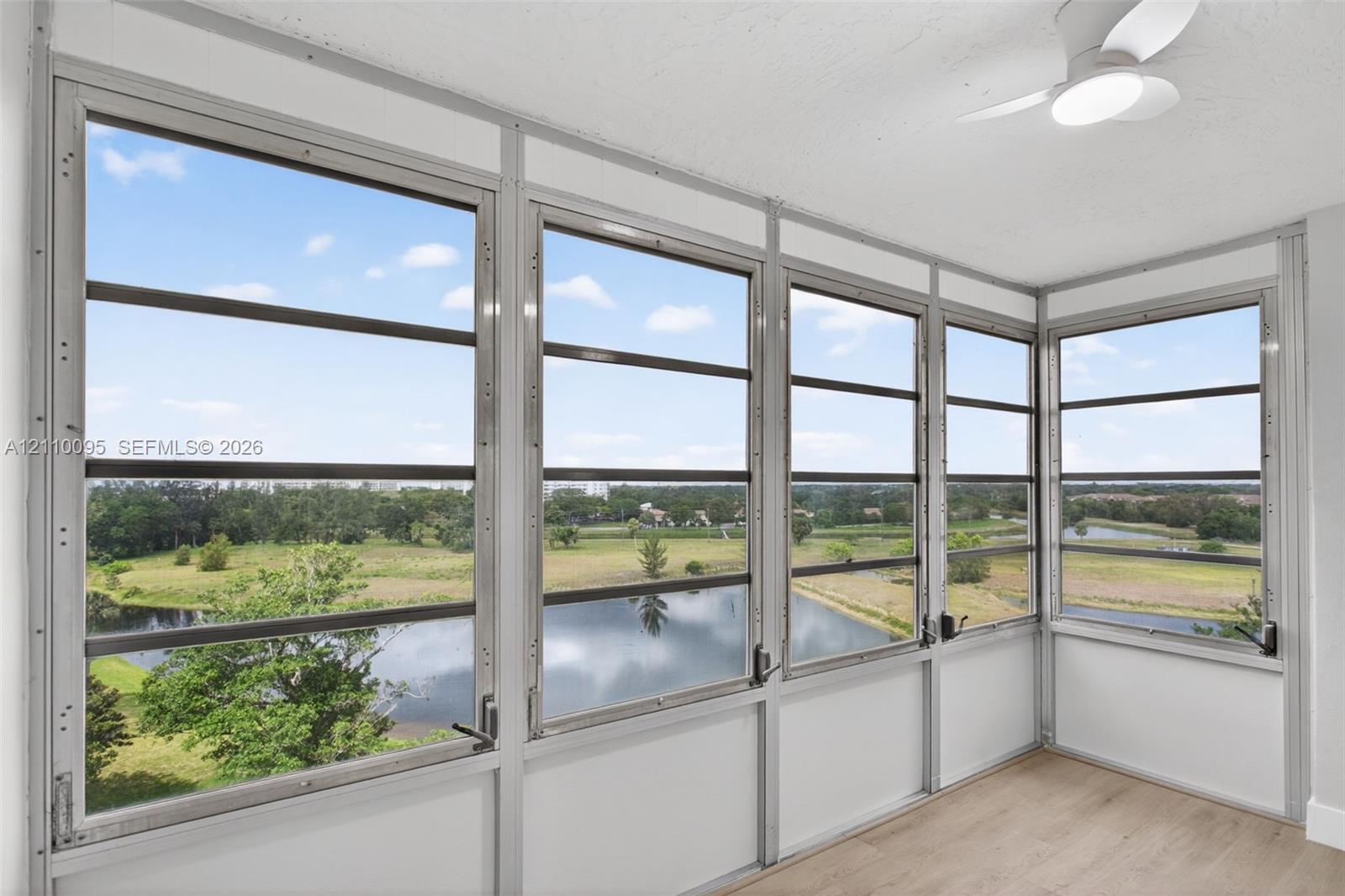 Floor-to-ceiling multi-panel windows, wood-finish flooring, and white ceiling fan