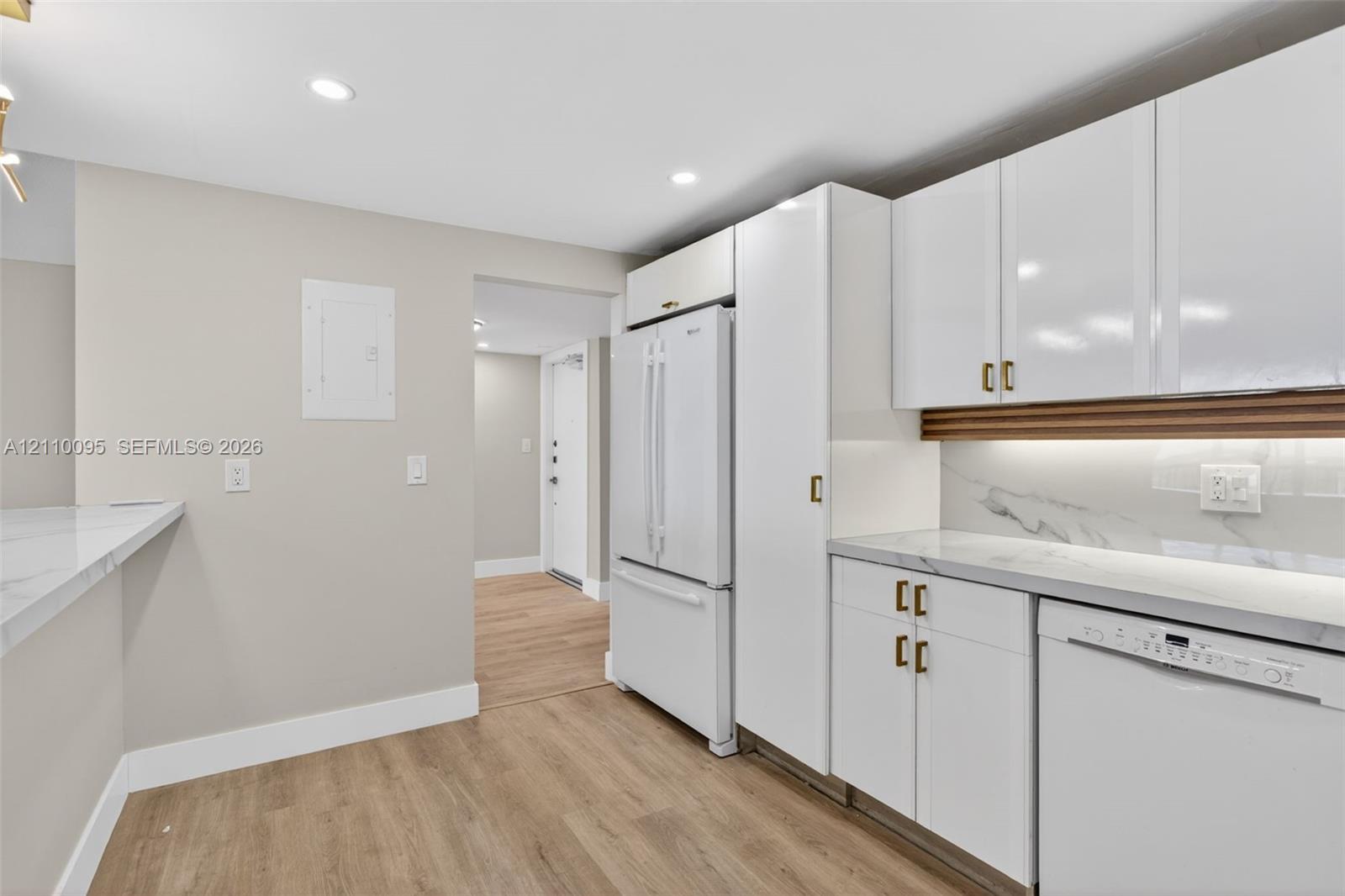 Kitchen featuring white cabinetry with gold-tone hardware, stone-finish countertops, under-cabinet lighting, recessed ceiling lighting, and wood-finish flooring