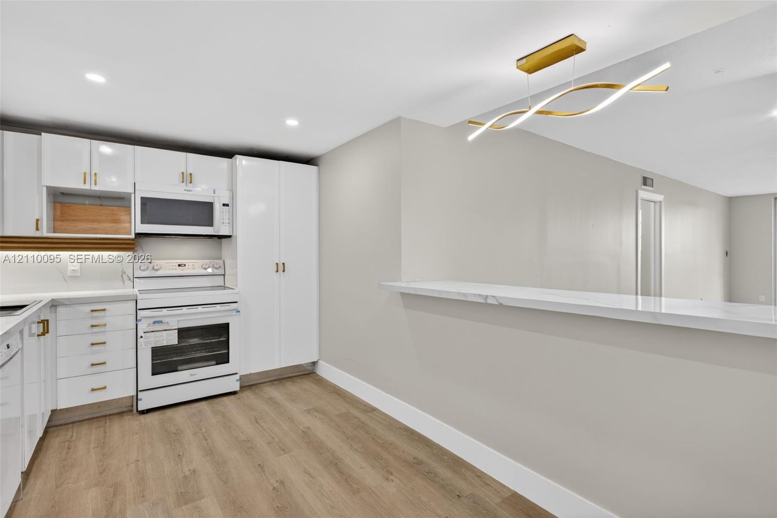 Kitchen featuring white high-gloss cabinetry, stone-surface breakfast bar, wood-finish flooring, recessed lighting, and contemporary gold-tone chandelier