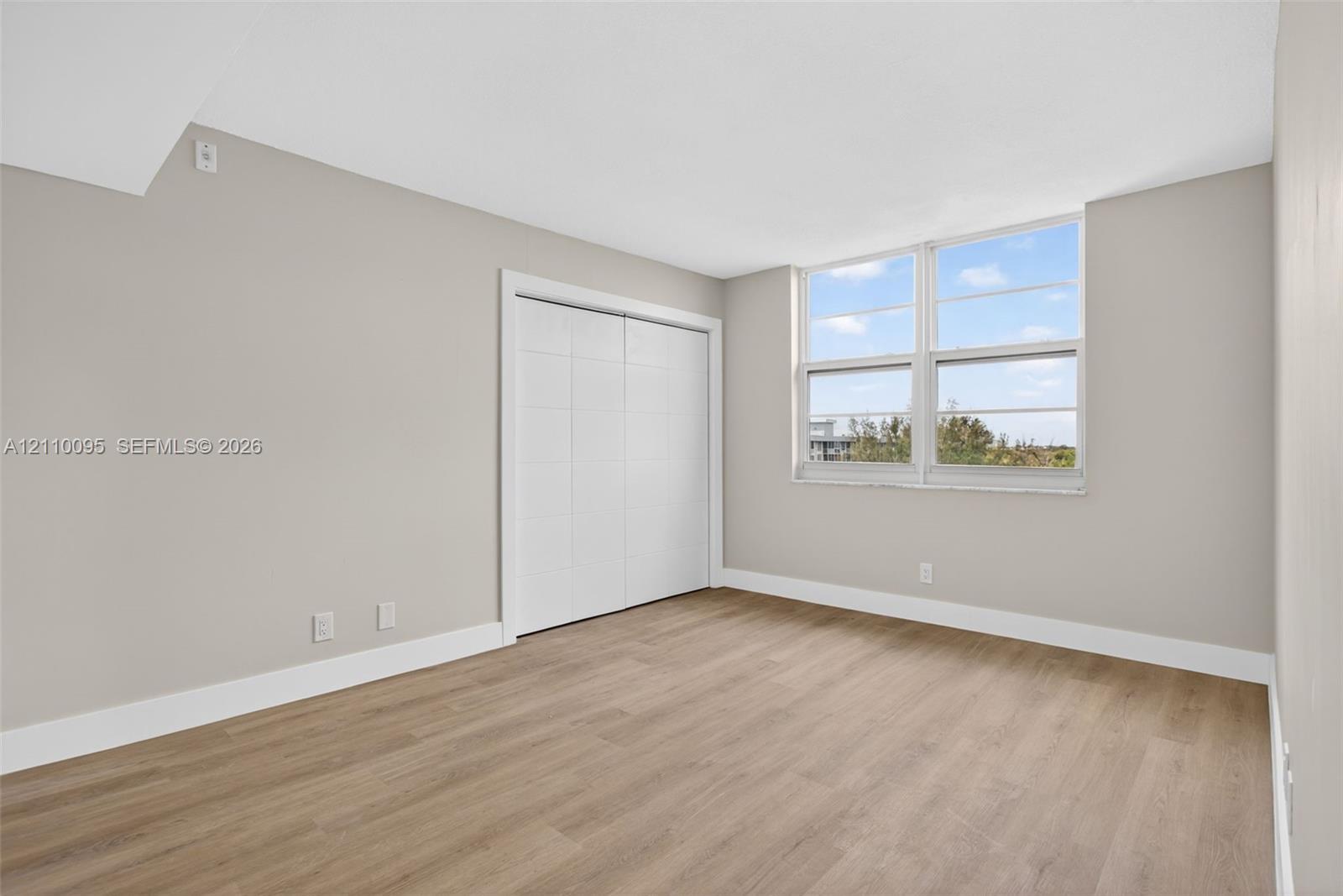 Neutral-toned interior featuring wood-finish flooring, dual-pane windows, and a built-in closet with sliding doors
