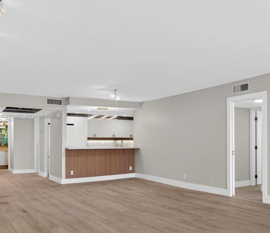 Open-concept interior featuring wood-finish flooring, a kitchen peninsula with vertical slat detailing, white cabinetry, and modern integrated pendant lighting