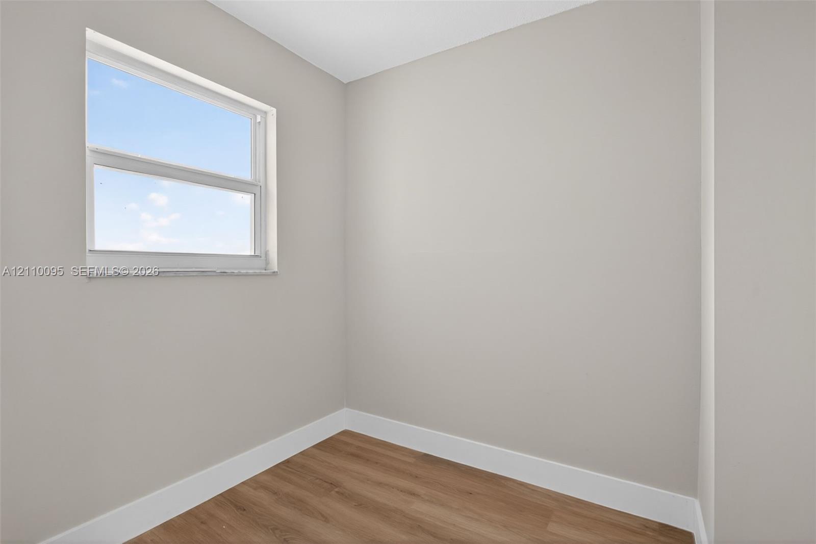 Neutral-toned interior space featuring wood-finish flooring and a single window with a stone sill