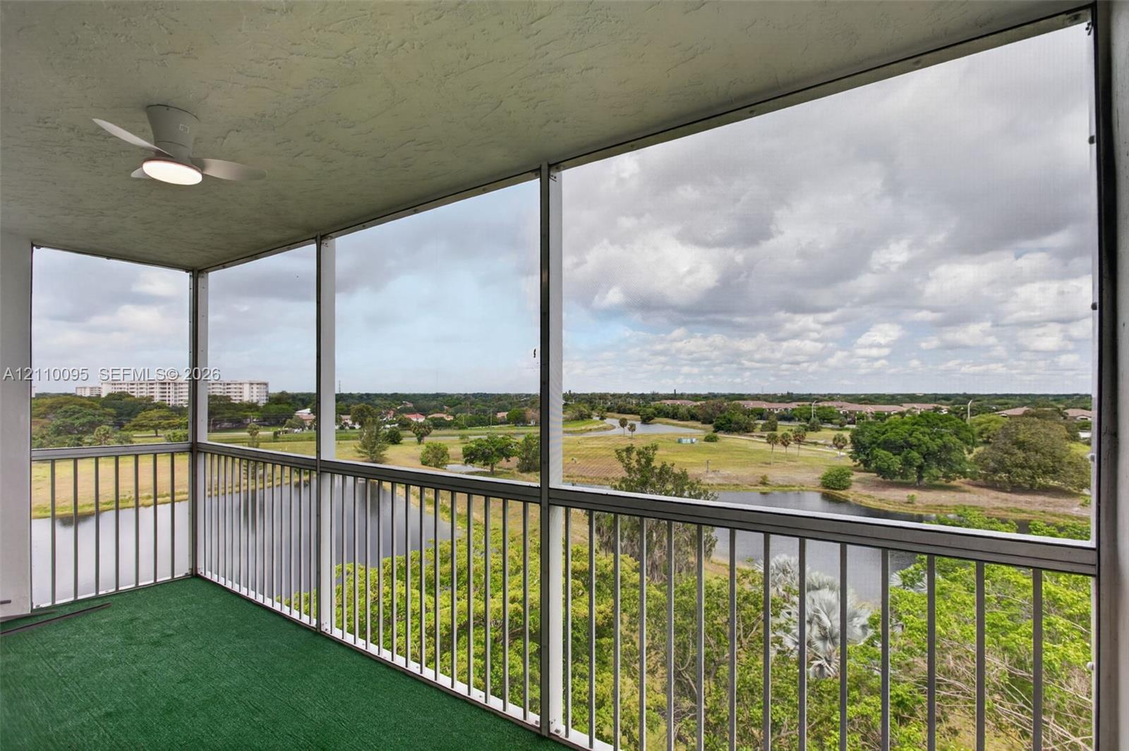 Screened-in balcony featuring a metal railing, ceiling-mounted light fixture, and an expansive outlook of the surrounding water and landscape