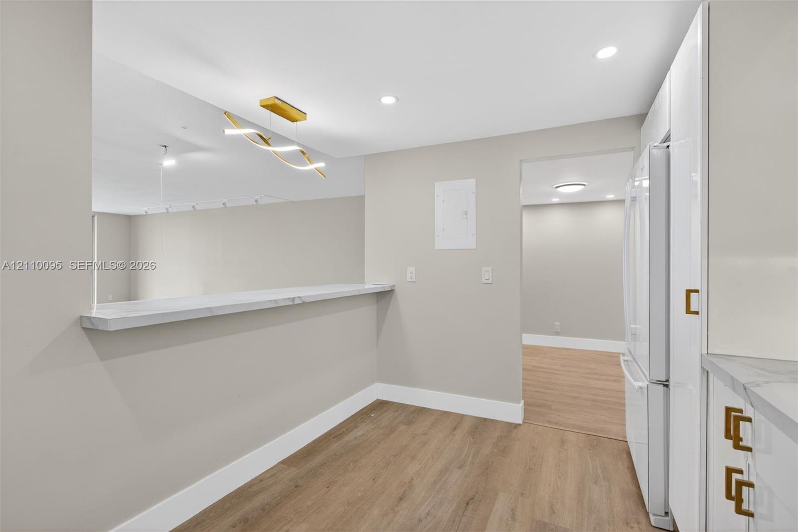 Kitchen featuring white cabinetry with gold-tone hardware, stone-finish countertops, wood-finish flooring, recessed lighting, and a modern sculptural pendant fixture