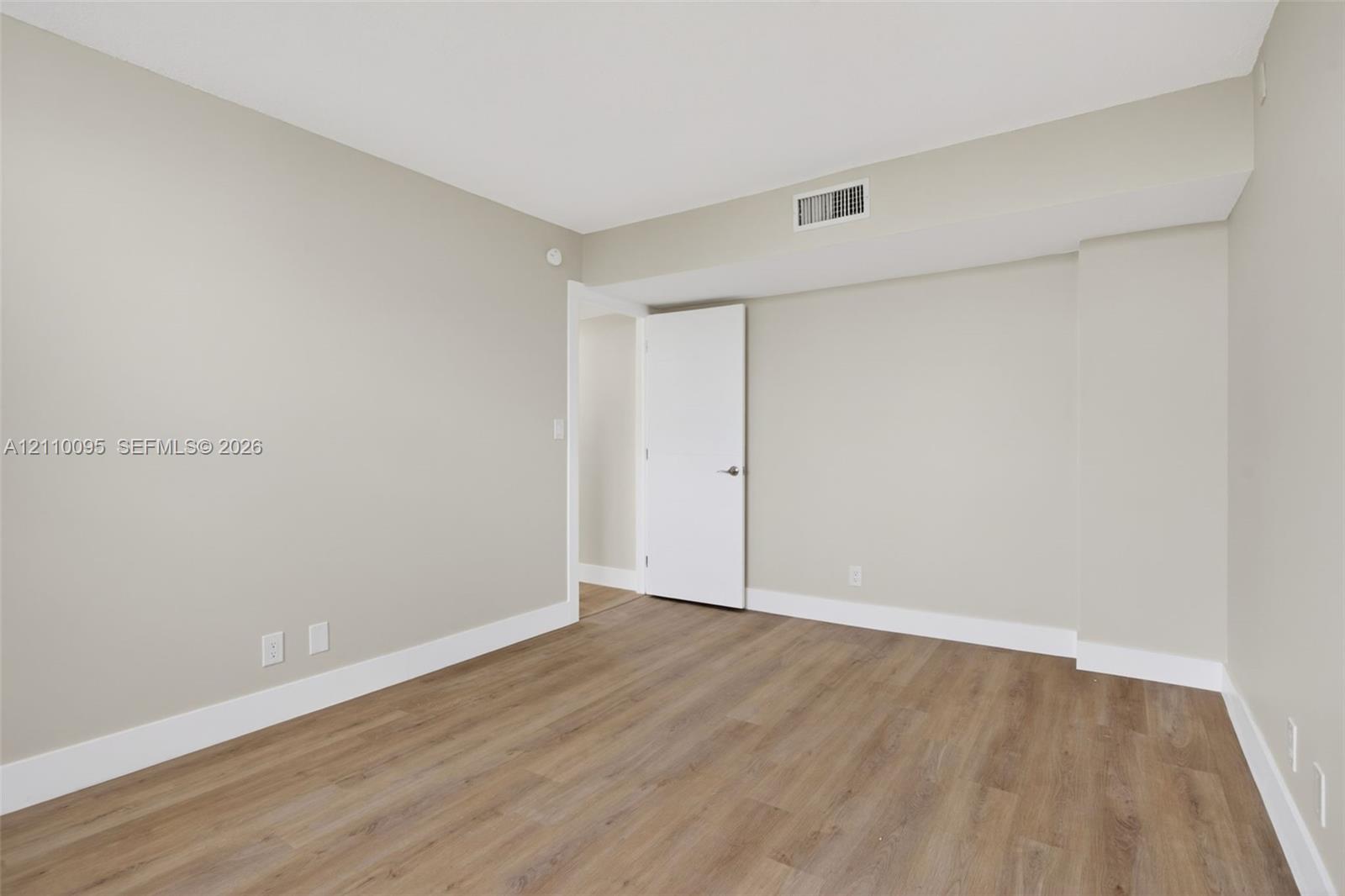 Neutral-toned interior space featuring wood-finish flooring, crisp white walls, and a solid-core interior door