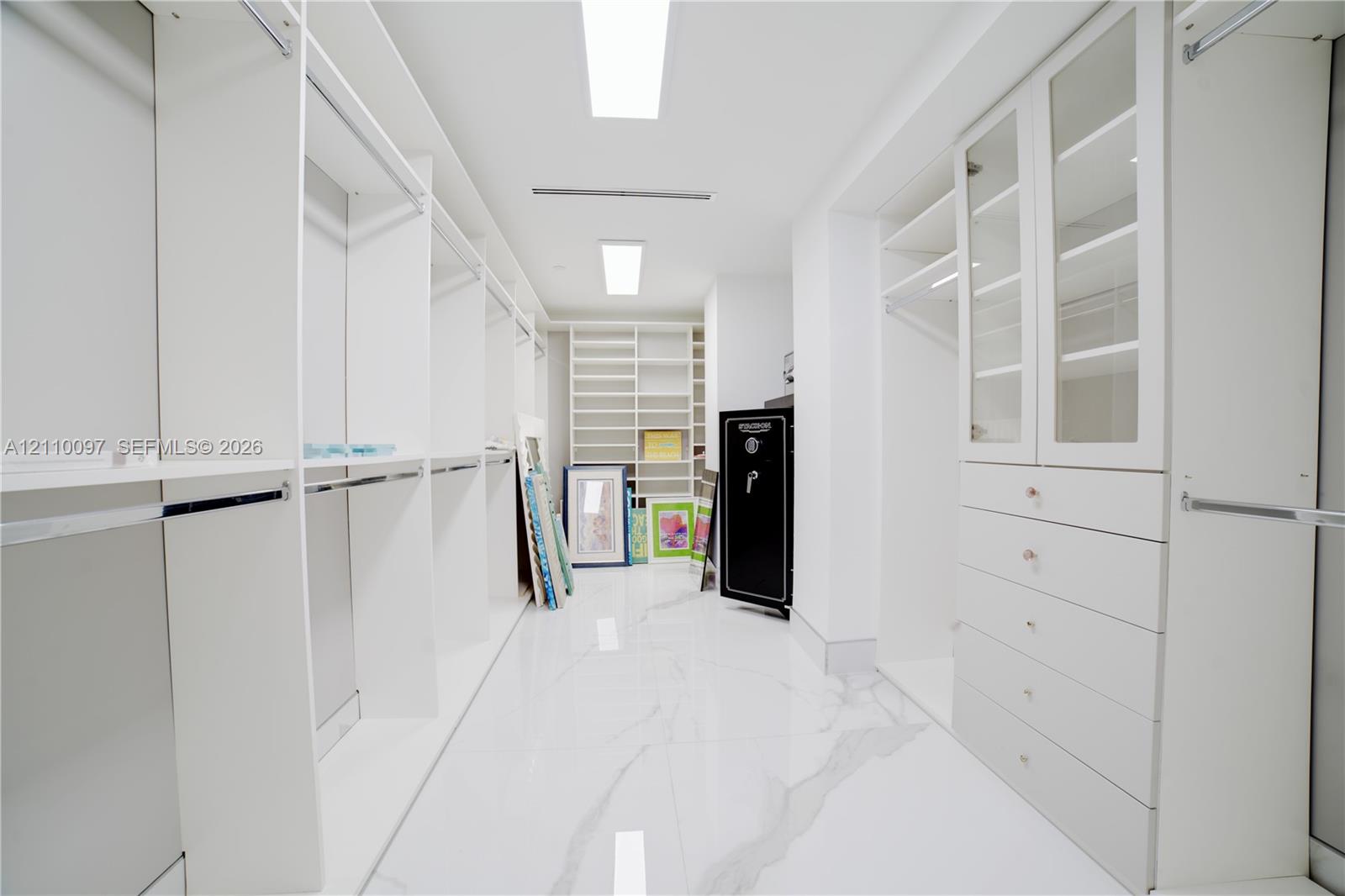 Walk-in closet featuring extensive built-in white cabinetry, glass-fronted upper doors, multiple storage drawers, and polished stone-finish flooring