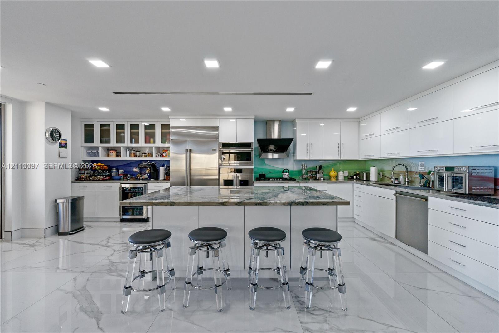 Modern kitchen featuring high-gloss cabinetry, a central island with natural stone countertop, stainless steel appliances, and large-format tile flooring