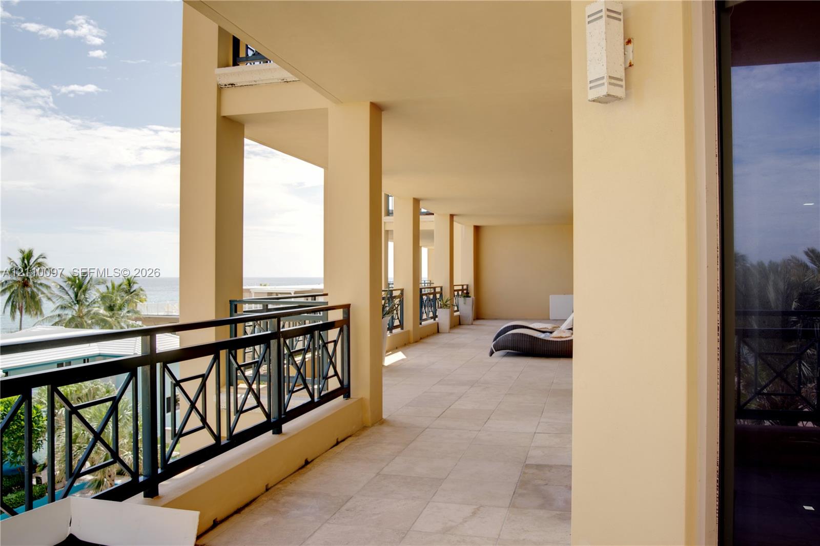 Covered terrace featuring stone-tile flooring, metal geometric railings, and mounted exterior lighting