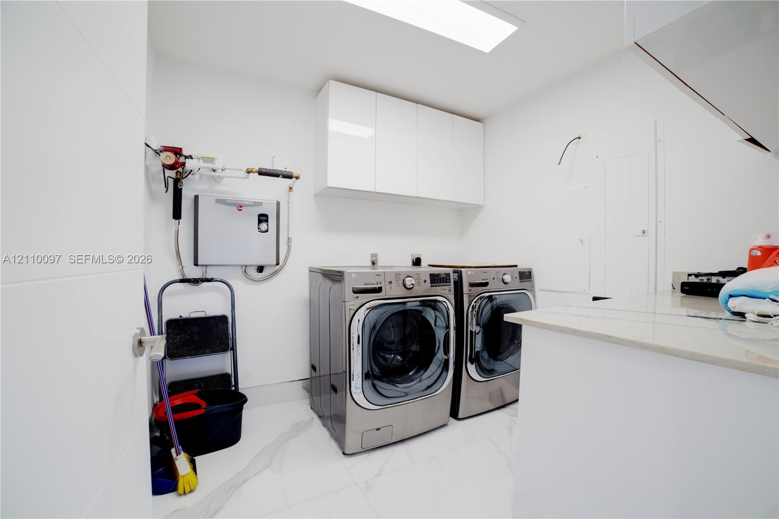 Laundry room featuring white high-gloss cabinetry, stone-finish countertops, and large-format tile flooring