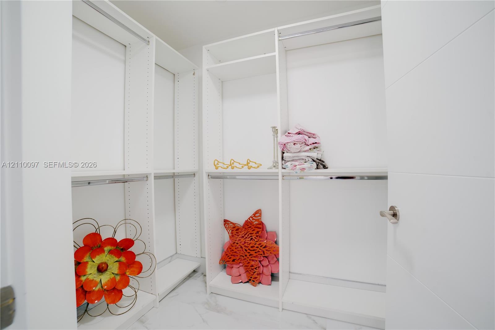Walk-in closet featuring white built-in shelving, adjustable storage cubbies, metal hanging rods, and stone-finish flooring