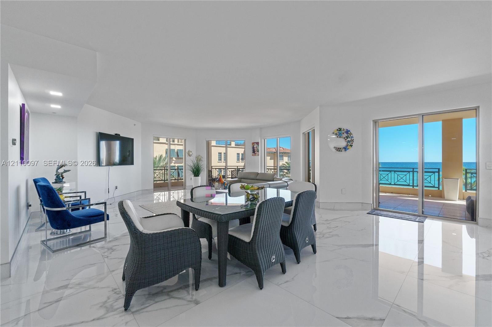 Open-concept living space featuring large-format stone-finish tile flooring, recessed lighting, and multiple sliding glass doors providing access to the exterior balcony with ocean scenery
